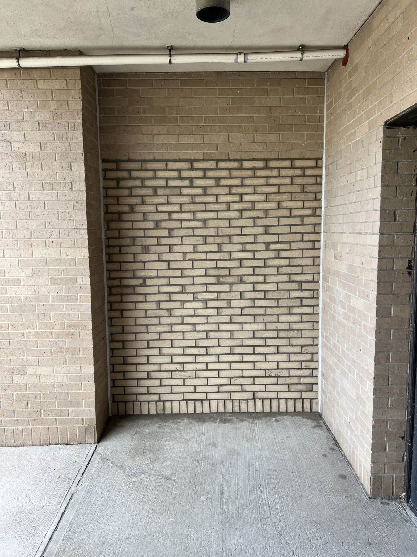 Tan brick wall with a rectangular infill panel of matched replacement brick and fresh mortar