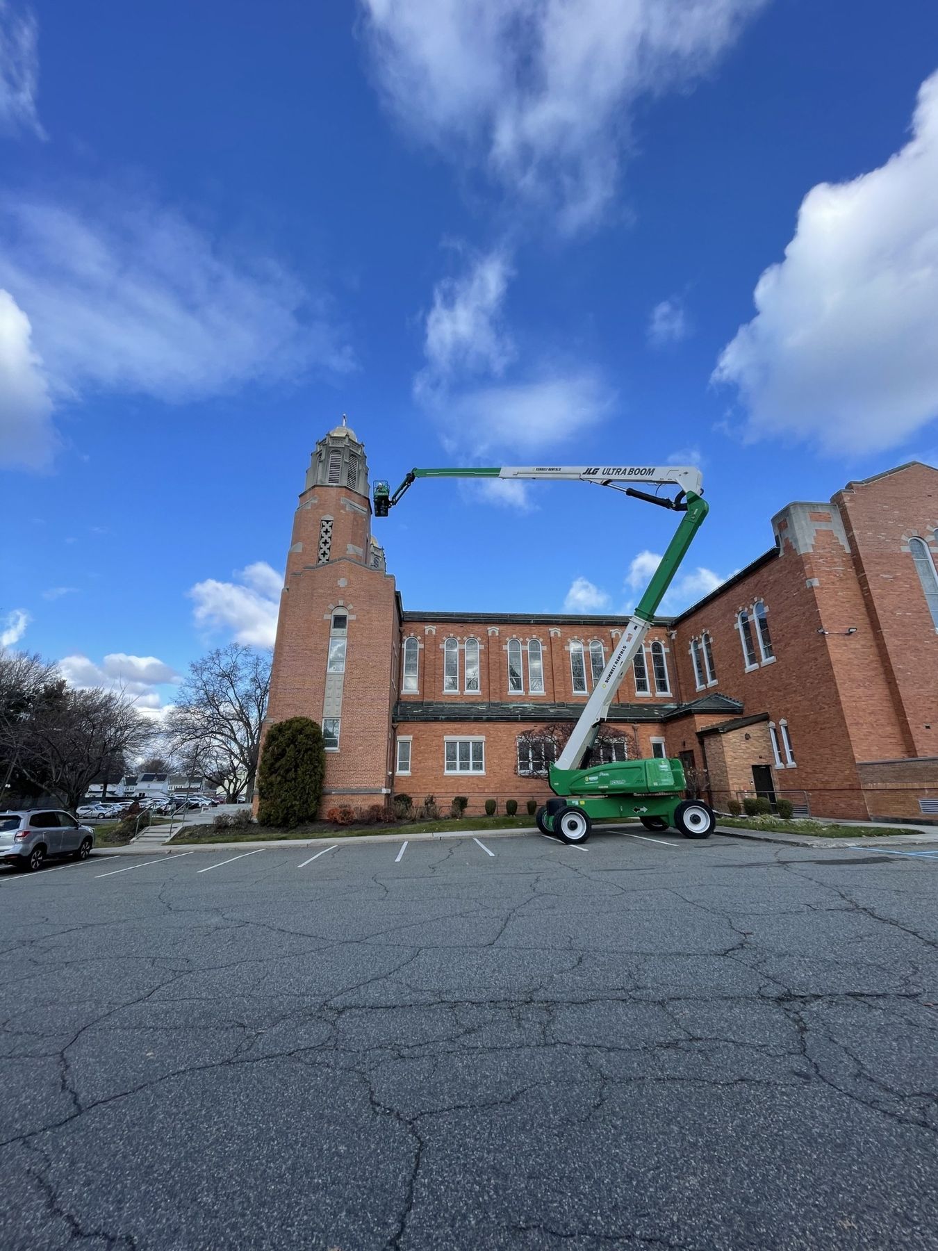 Boom lift extended to the top of a historic red brick church belltower during stone and mortar restoration