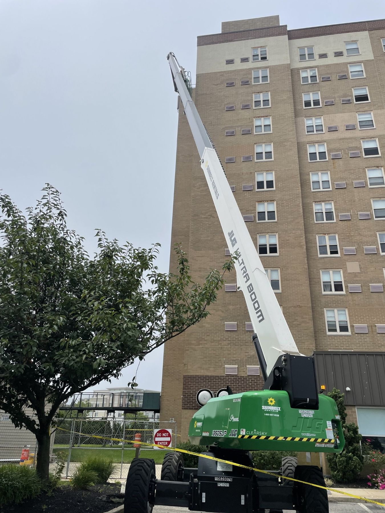Boom lift reaching the upper floors of a tall beige brick apartment building for facade repairs