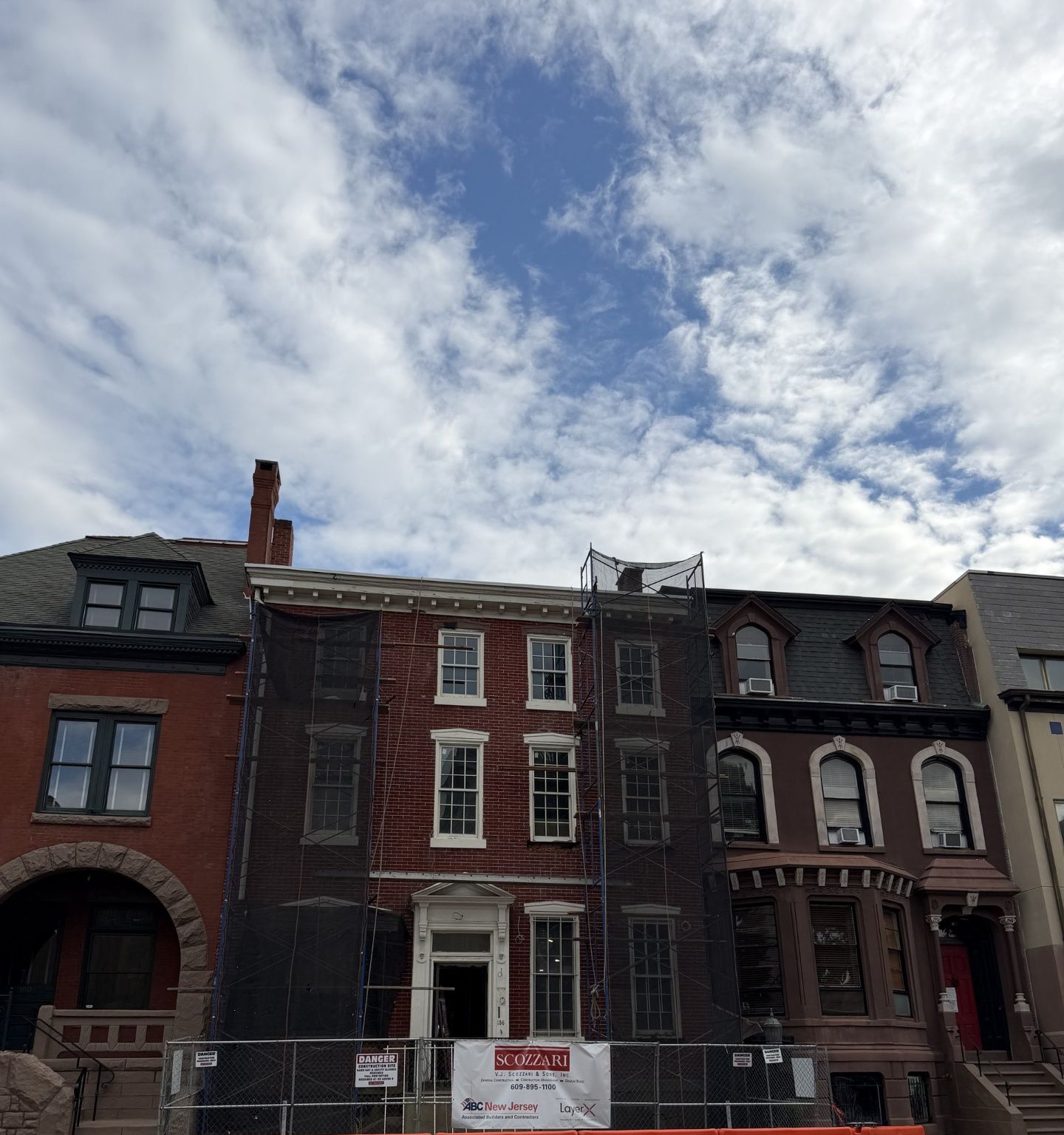 Historic red brick townhouse under facade restoration with scaffolding and protective mesh