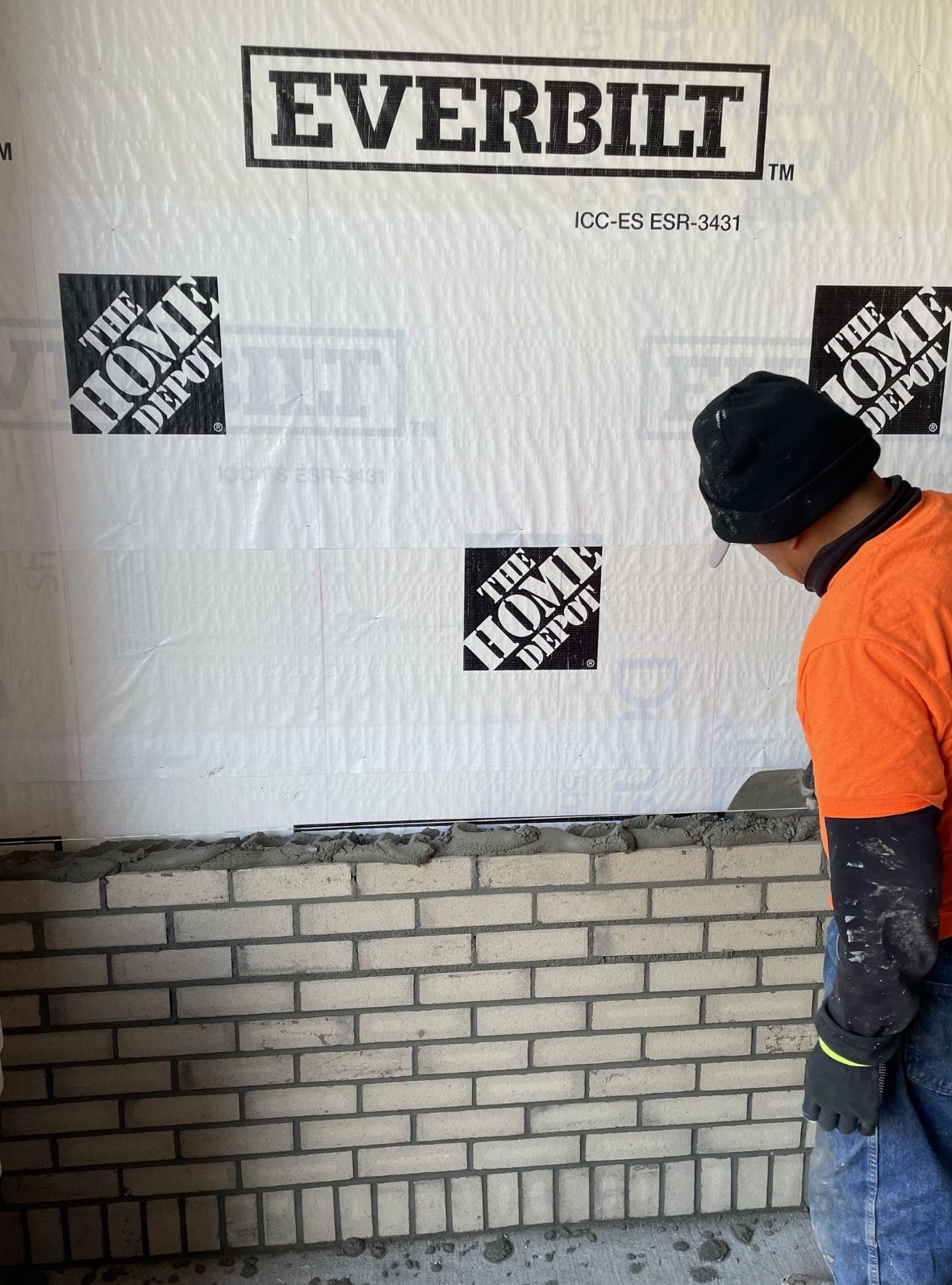Yarussi mason in a company shirt hand-laying a course of brick against a prepared wall