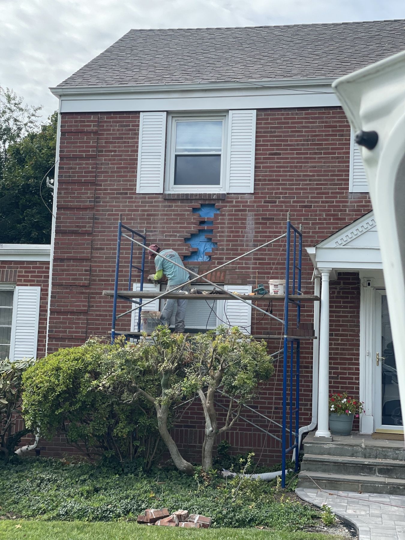 Mason on scaffolding repairing brickwork across the facade of a two-story red brick family home